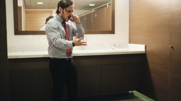 Furious Business Man Screaming On Cell Phone In Office Restroom